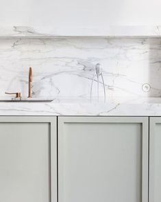 a kitchen with marble counter tops and white cupboards, gold faucet handles