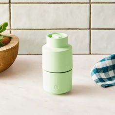 a green cup sitting on top of a counter next to a potted plant