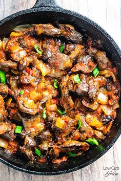 a skillet filled with meat and vegetables on top of a wooden table