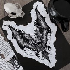 a black and white drawing of a bat on a piece of paper next to a skull