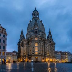 an old building is lit up at night with people walking around it and buildings in the background