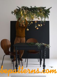 a table and chairs with christmas decorations hanging from the ceiling above it, in front of a black wall