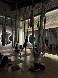 people doing yoga in a large room with mirrors on the wall and hanging hammocks