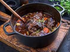 a pot filled with meat and vegetables on top of a wooden cutting board