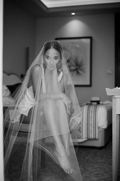 black and white photograph of a woman wearing a veil on her head sitting on a bed