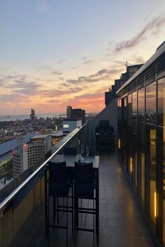 a balcony with tables and chairs overlooks the city skyline at sunset or dawn,