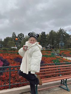 a woman standing on a bench in front of a flower garden holding a coffee cup