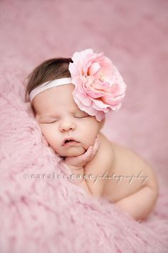 a baby is sleeping on a pink blanket with a flower in her hair