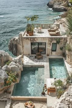 an outdoor swimming pool next to the ocean with chairs and tables on it, surrounded by large rocks