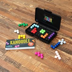 an open black case filled with colorful candies on top of a wooden table next to a book