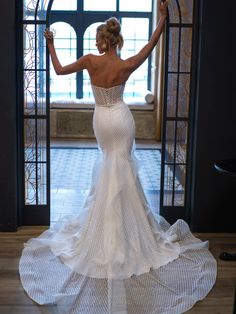 a woman standing in front of a doorway wearing a wedding dress with an open back