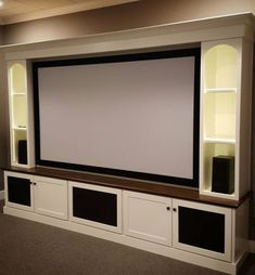 a large screen mounted to the side of a wall in a living room with built - in shelving