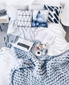 a bed with pillows and blankets on top of it, next to a laptop computer