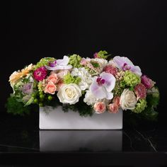 an arrangement of flowers in a white vase on a black table with a dark background