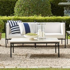 a white couch sitting on top of a gravel covered ground next to a table and chairs