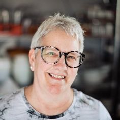 an older woman with glasses smiling at the camera while wearing a t - shirt and looking into the camera