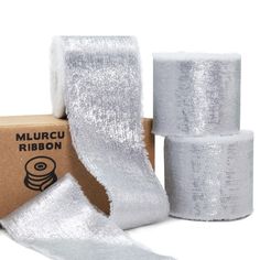 three rolls of silver glitter ribbon next to a cardboard box with white tape on it