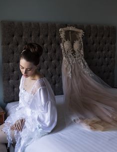 a woman sitting on top of a bed next to a wedding dress