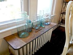 there are many glass vases on the table by the window and in front of the radiator