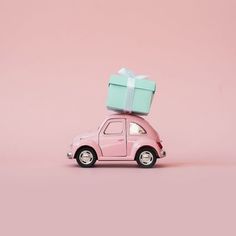 a small pink car with a green box on the roof and a bow on top