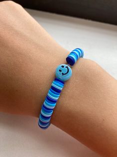 A clay bead, also known as heishi bead bracelet based off the blue smiley face charm. Blue Heishi Beads Friendship Bracelets, Fun Blue Beaded Friendship Bracelets, Playful Blue Friendship Bracelets With Colorful Beads, Blue Fun Friendship Bracelets With Colorful Beads, Blue Playful Friendship Bracelets, Casual Blue Heishi Beads Bracelet, Casual Blue Heishi Beaded Bracelets, Casual Blue Evil Eye Bracelet With Round Beads, Playful Blue Friendship Bracelets