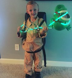 a little boy that is standing in front of a chair with some string lights on