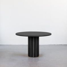 a black round table sitting on top of a cement floor next to a white wall