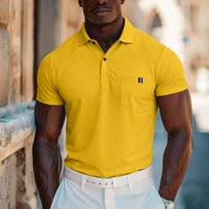 a man wearing a yellow polo shirt and white pants standing next to a stone wall