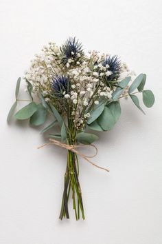 a bouquet of white flowers and greenery tied with twine on a white wall