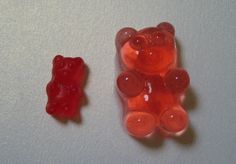 two gummy bears sitting next to each other on a white surface with one red gummy bear in the foreground