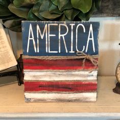 a wooden block with the word america painted on it and an american flag in the background