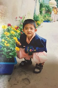 a young boy kneeling next to a potted plant