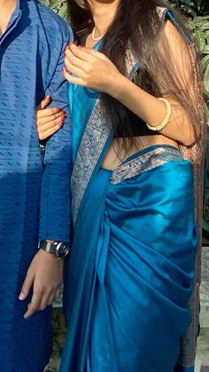 a man and woman standing next to each other in blue sari dresses, smiling at the camera