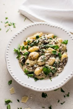 a white bowl filled with pasta covered in mushrooms and spinach sprinkled with parsley