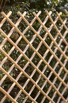 a close up of a wooden fence with bushes in the backround behind it