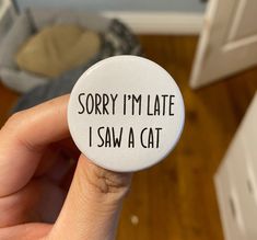 someone holding up a button that says sorry i'm late i saw a cat