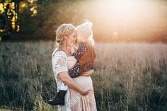 a woman holding a baby in her arms while standing in a field with tall grass