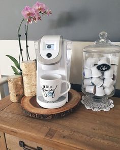 a coffee maker sitting on top of a wooden table next to a vase filled with flowers