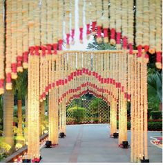 an archway decorated with red and white flowers in the middle of a walkway surrounded by greenery