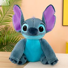 a blue stuffed animal with purple ears sitting on a table next to a potted plant