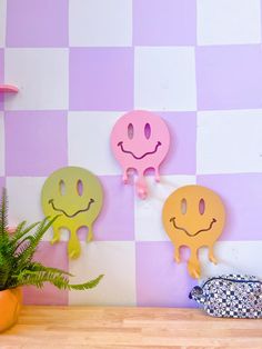 three smiley faces are hanging on the wall next to a potted plant in front of a purple and white checkered wall