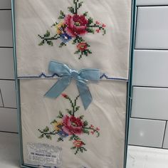 two cross stitched towels with blue bows and flowers on them are hanging from the wall