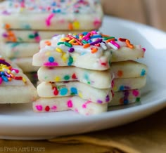 white cookies with sprinkles and colored frosting are on a plate, ready to be eaten