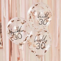 three clear balloons with the number 30 printed on them and some confetti around it