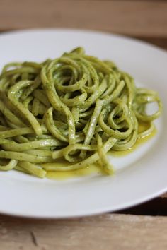 a white plate topped with pasta covered in pesto sauce on top of a wooden table