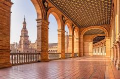 an empty walkway with arches and clock tower in the background