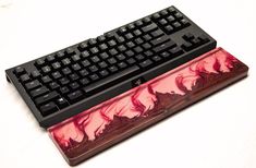 a computer keyboard sitting on top of a wooden desk next to a mouse pad with red and black designs