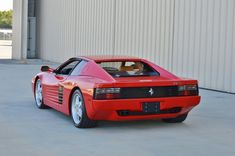 a red sports car is parked in front of a white building with a door open