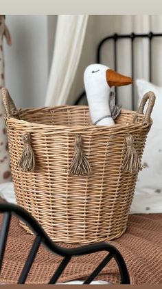 a wicker basket sitting on top of a bed next to a stuffed duck in it