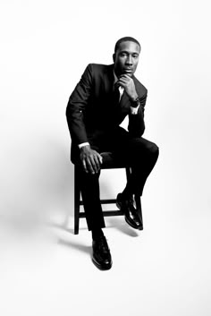 a black and white photo of a man in a suit sitting on a chair with his hand under his chin